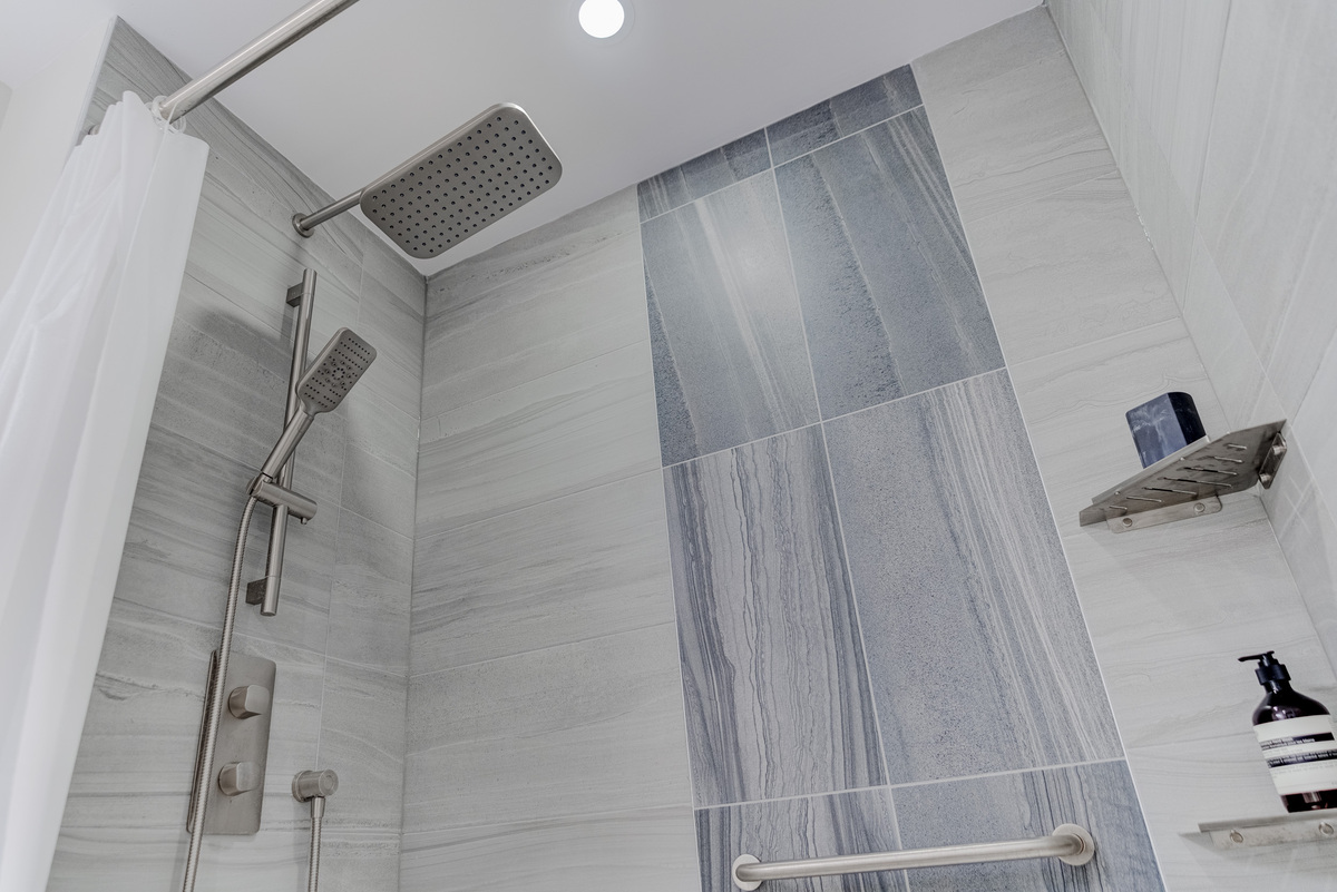 Large format tiling in GTA condo bathroom renovation with multi-shower heads and shelving