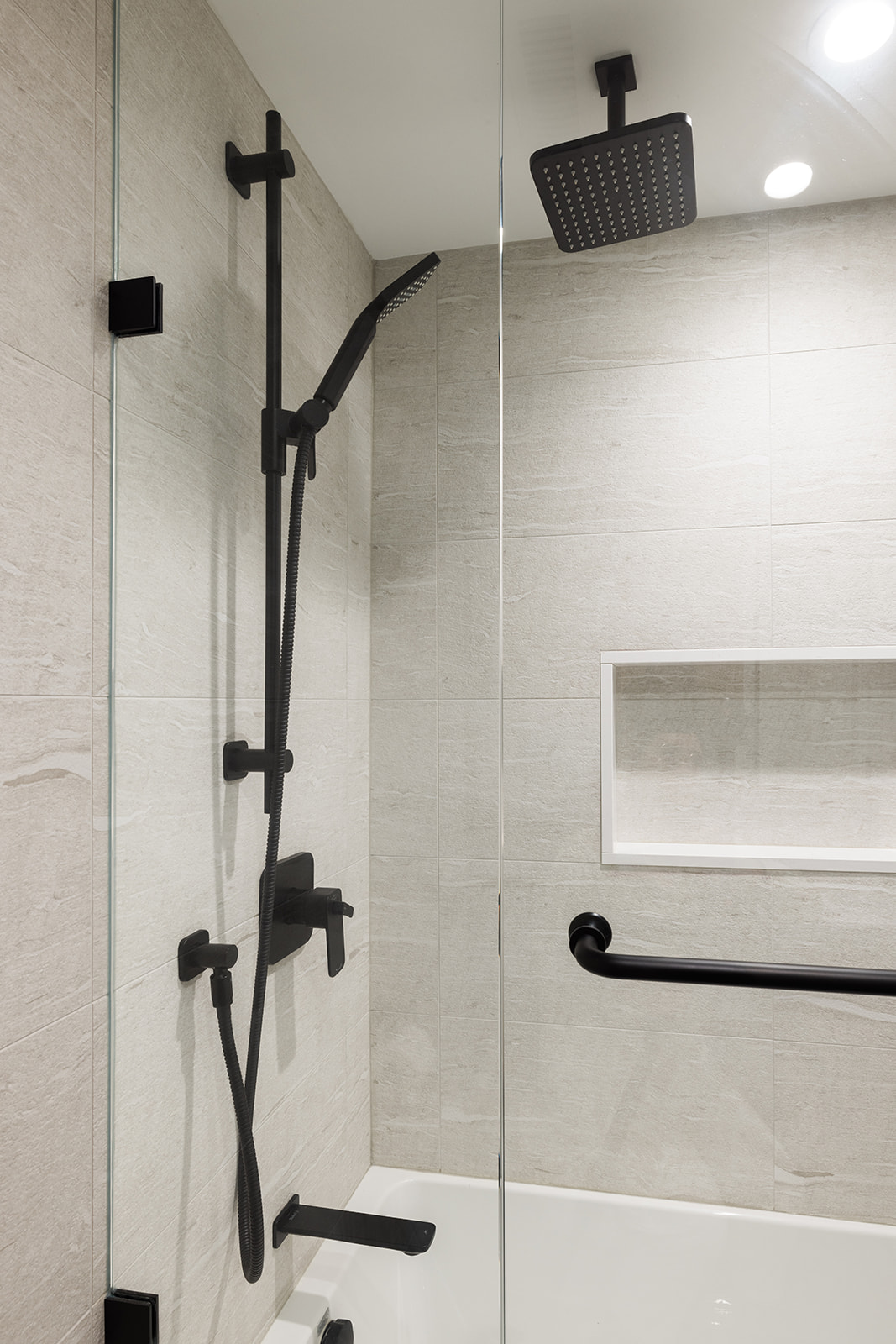Black shower fixture in condo walk-in shower renovation in downtown Toronto with inset shelving