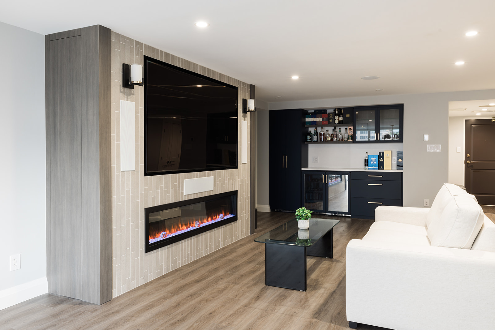 View of custom fireplace with mounted TV above in living room in downtown Toronto condo renovation with view of beverage station 